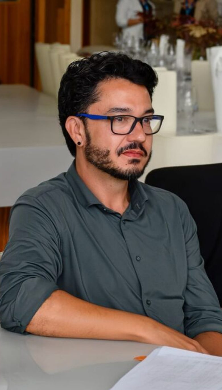 João Toledo em retrato, camisa cinza, olhando para a câmera